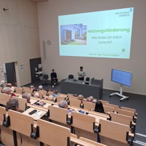 Professor Vaidya präsentiert einem Raum voller Zuschauer seine Slideshow zum Thema Heizungsförderung